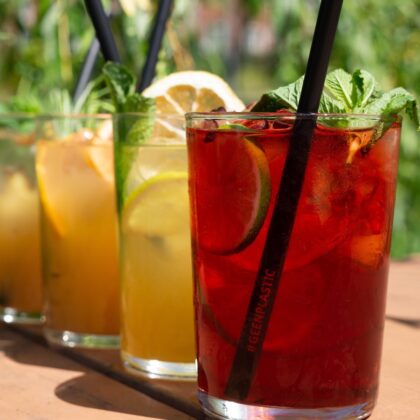 Je ziet vier kleurrijke drankjes met een rietje erin op een zonnige dag